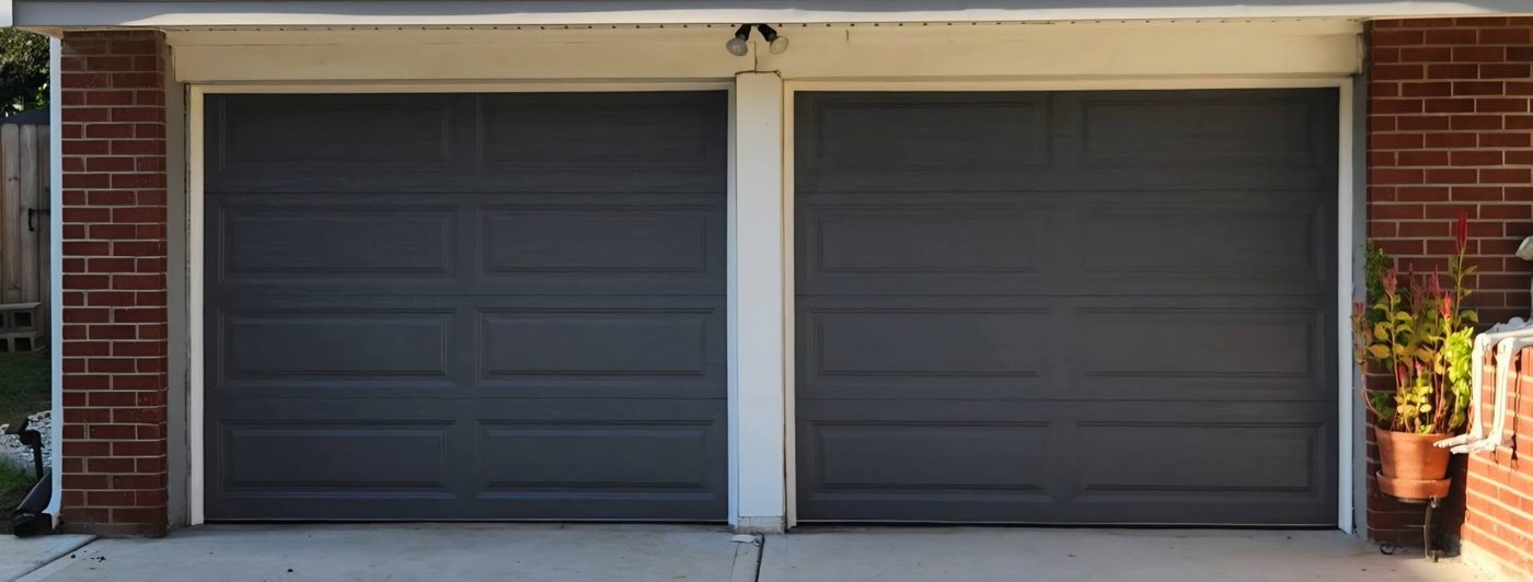 Two dark gray garage doors on a brick home